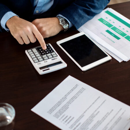 Close-up of insurance agent calculating costs while his clients is signing a contract in the office.