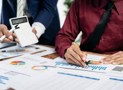 Two people are working on a project, one of them is writing on a piece of paper with a pen