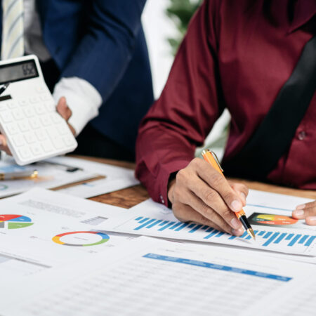 Two people are working on a project, one of them is writing on a piece of paper with a pen