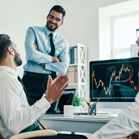 Working with investments. Group of young modern men in formalwear analyzing stock market data while working in the office