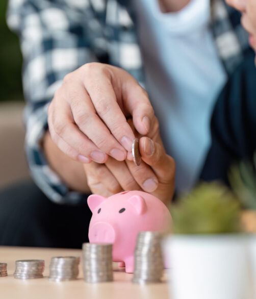 A loving LGBTQ couple focused on their savings as they carefully place coins into a pink piggy bank, illustrating their commitment to financial growth in a warm home environment.