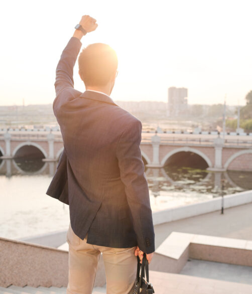 Rear view of young business student standing with raised arm and looking at city, he ready to be successful